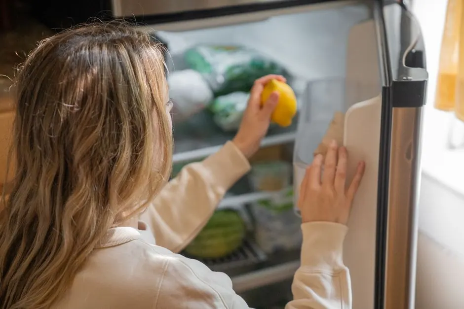 Woman reaching for a lemon in the fridge, illustrating healthy living habits.
