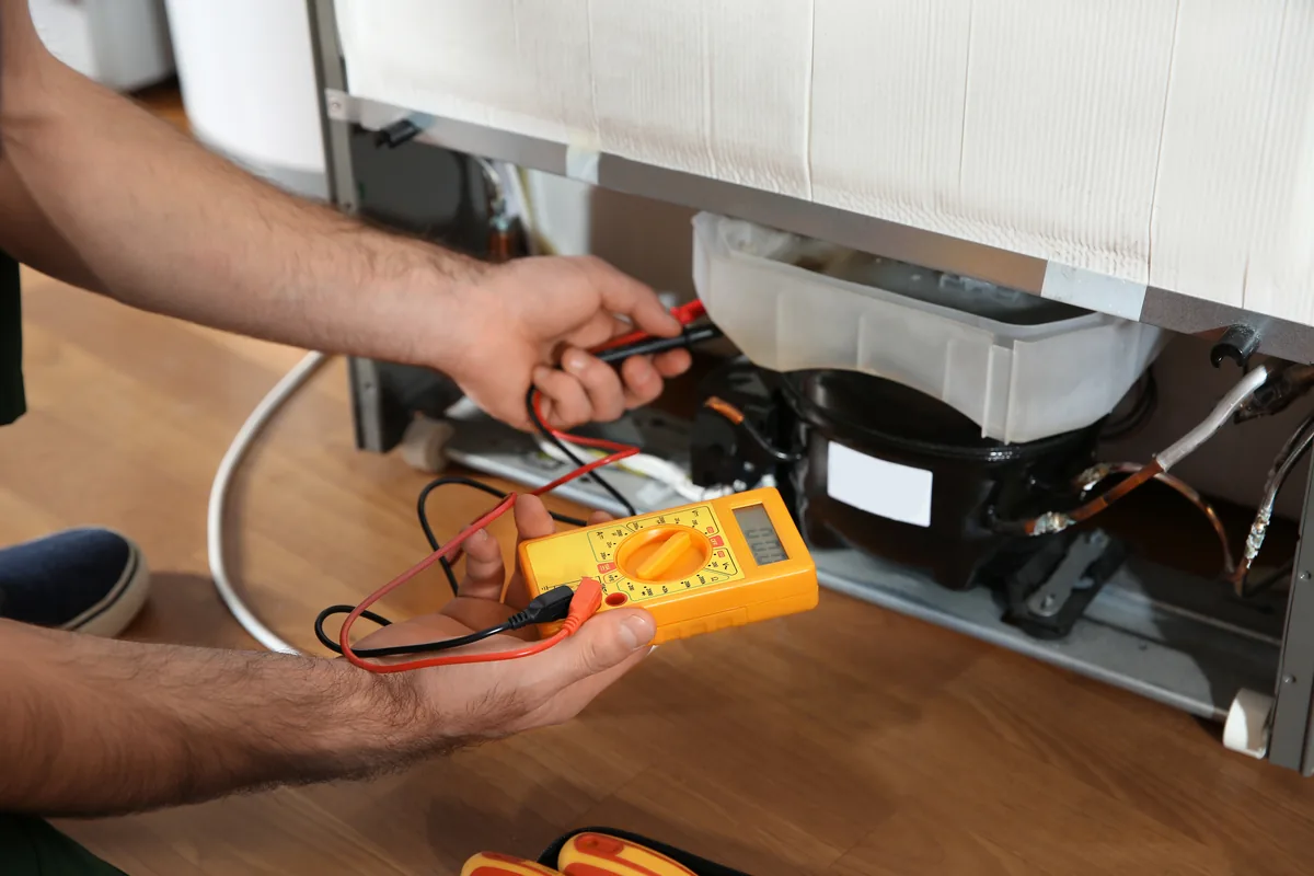 Technician testing a refrigerator compressor with a multimeter