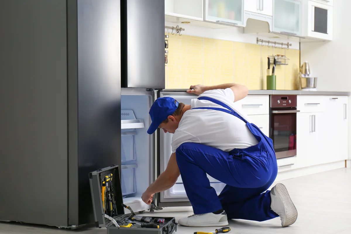 Technician repairing a refrigerator in a home kitchen