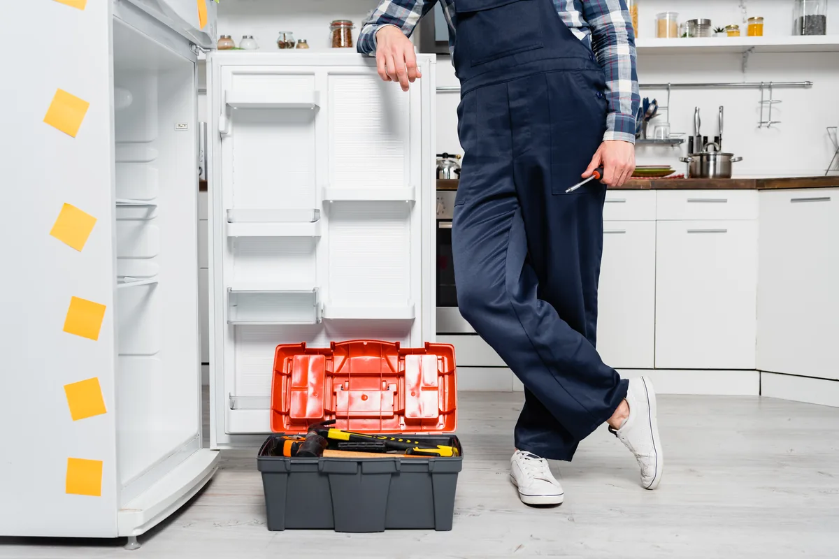 Repair technician with a toolbox beside an open refrigerator