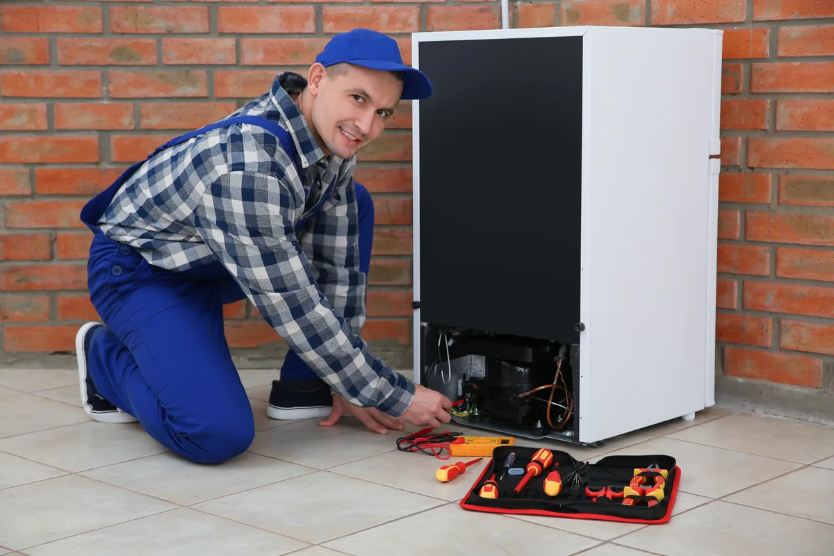 Smiling appliance technician repairing a refrigerator