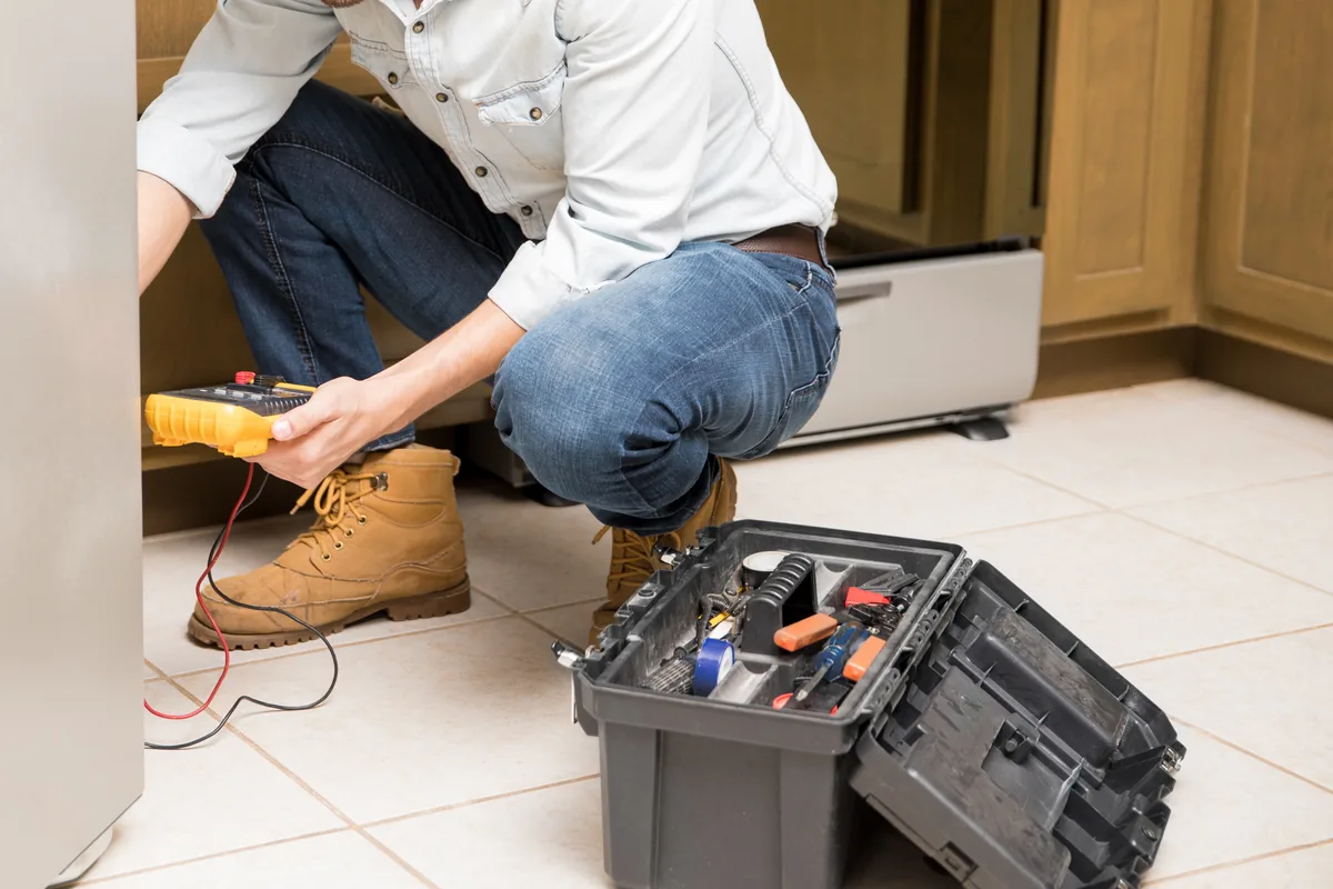 Technician with a toolbox kneeling beside a refrigerator