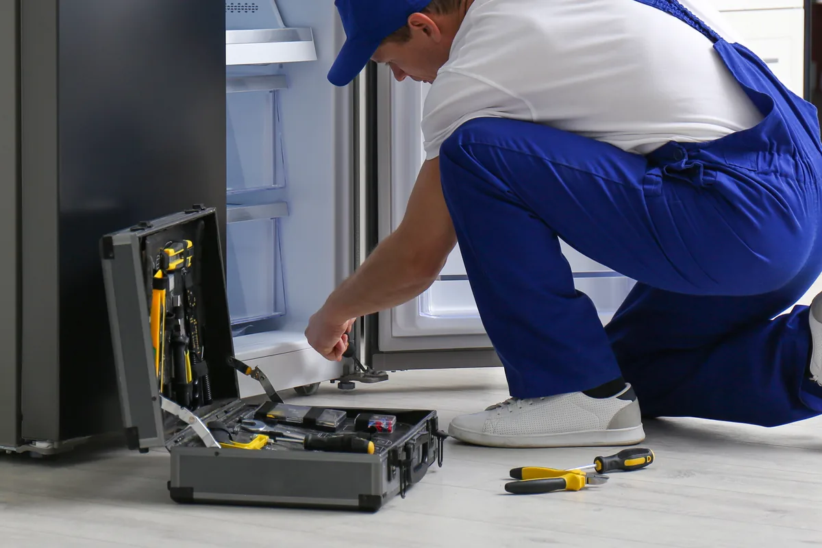 Repair technician toolbox on a kitchen floor beside a refrigerator