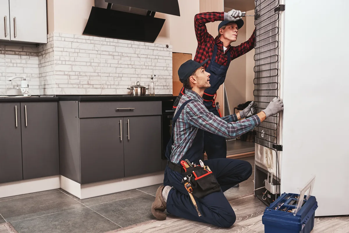 Two technicians repairing a refrigerator in a home kitchen
